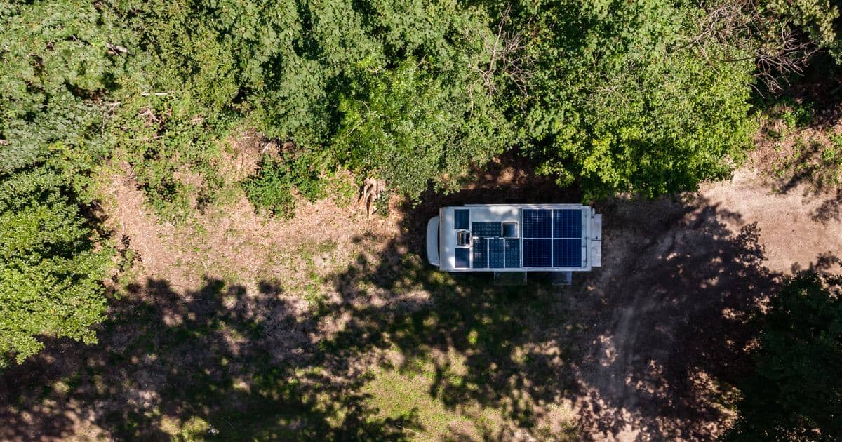 Aerial view of a camper van with roof solar panels parked in a forest clearing